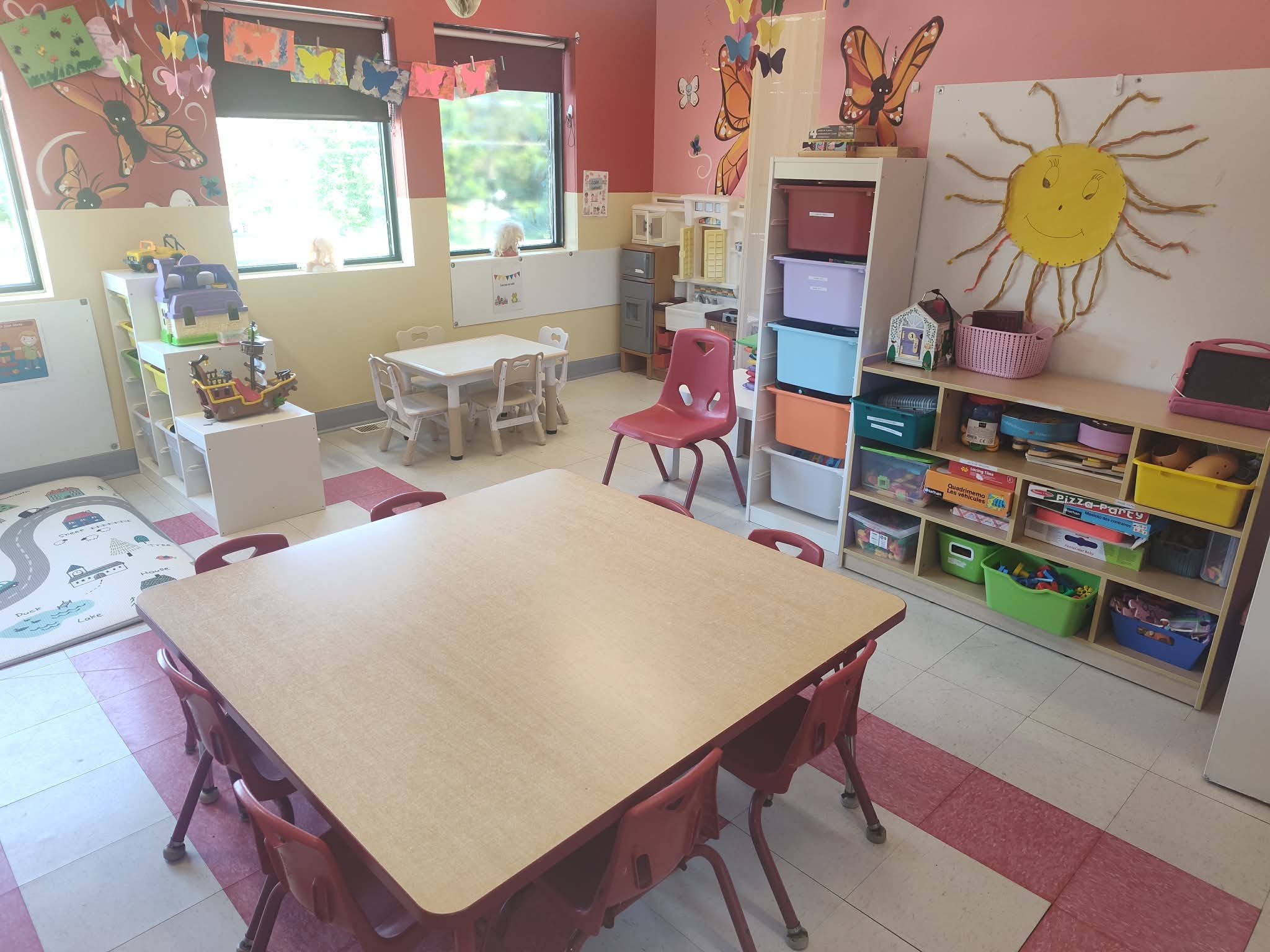 Salle de groupe lumineuse avec tables et espaces de jeux éducatifs